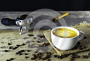 Cup of hot black coffee with a nice crema on top with a pile of roasted coffee beans and portafilter on old wooden background