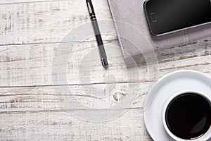 Cup of hot black coffee and note book, pen on wood table