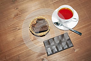 Cup with hot black tea and dark chocolate on a wooden table background close-up