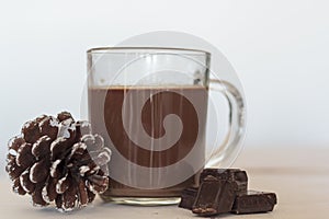 Cup of hot chocolate with chocolate pieces and pine cone on the side