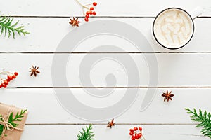 Cup of hot chocolate with marshmallow, fir tree branches, gift, red berry, Christmas decorations on wooden white background. Flat