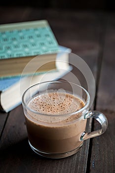 Cup of hot chocolate on a wooden table next to books.