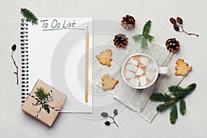 Cup of hot cocoa or chocolate with marshmallow, cookies and notebook with christmas to do list on white table from above.