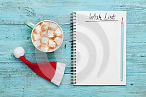 Cup of hot cocoa or chocolate with marshmallow, Santa Claus hat and notebook with wish list, christmas planning concept. Flat