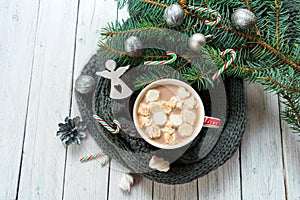 A cup of hot cocoa or chocolate with marshmallows on a background of a knitted scarf and a branch of a Christmas tree. A tradition