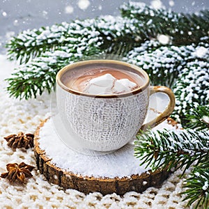 Cup of hot cocoa or hot chocolate on knitted background with fir tree and snow effect, traditional beverage for winter time
