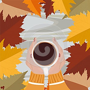 Cup of hot cocoa in woman`s hands holding it over wooden autumn background with leaves. Top view. Warm drink concept