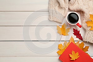 Cup of hot coffee, book, sweater and autumn leaves on white wooden table, flat lay. Space for text