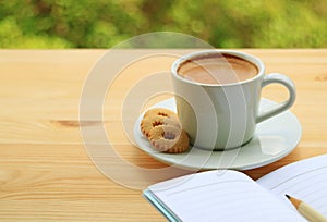 Cup of Hot Coffee and Cookies with Lined Note Papers on Wooden Table with Blurry Green Foliage