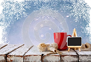 Cup of hot coffee and cozy knitted scarf and blackboard on wooden table