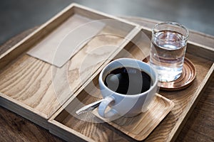 A cup of hot coffee and a glass of water in vintage wooden tray on the table in cafe