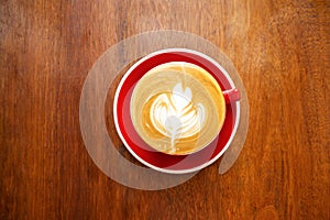 Cup of hot coffee with latte art in leaf shape on wooden table. Top view.