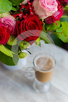 Cup of hot coffee with milk stands near the window and a bright colored bouquet of flowers