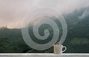 Cup of hot coffee with and smoke on balcony in the morning. Fog and mountains