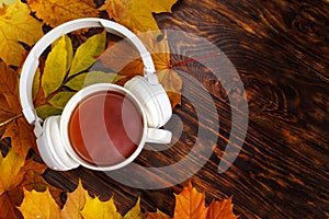 A Cup of hot coffee or tea with autumn leaves and headphones on a brown wooden background