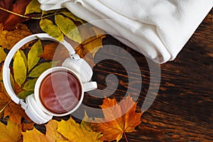 A Cup of hot coffee or tea with autumn leaves and headphones on a brown wooden background