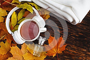 A Cup of hot coffee or tea with autumn leaves, plaid, bottle of perfume and headphones on a brown wooden background