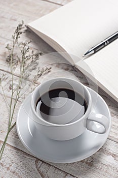 Cup of hot coffee and white note book on white wood table for happy time