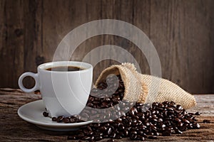 A cup of hot coffee on a wooden table with roasted coffee beans