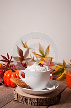 Cup of hot creamy cocoa with froth with autumn leaves and pumpkins on the background