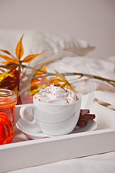 Cup of hot creamy cocoa with froth on the white tray with autumn leaves and pumpkins on the background