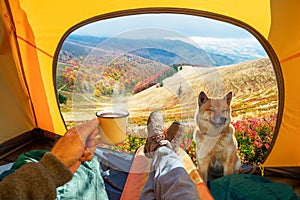 Cup of hot drink in the hand and wonderful view of autumn mountain tops through the open entrance of the tent. The beauty of a
