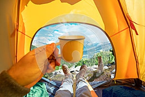 Cup of hot drink in the hand and wonderful view of mountain tops through the open entrance to the tent. The beauty of a romantic