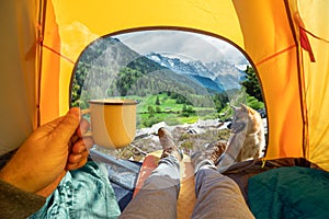 Cup of hot drink in the hand and wonderful view of snowy mountain tops through the open entrance of the tent. The beauty of a