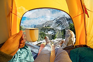 Cup of hot drink in the hand and wonderful view of snowy mountain tops through the open entrance of the tent. The beauty of a