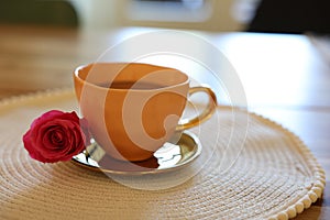 Cup of hot drink and red rose on table indoors, closeup. Space for text