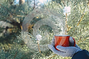 A cup of hot drink tea, coffee or mulled wine in winter nature. Female hand with a red cup. Winter relax comfort and mood