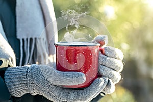 A cup of hot drink tea, coffee or mulled wine in winter nature. Female hand with a red cup. Winter relax comfort and mood