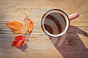 Cup with hot drink on a wooden table near autumn leaves