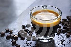 Cup of hot espresso with a nice crema on a rustic concrete table with a pile of roasted arabica coffee