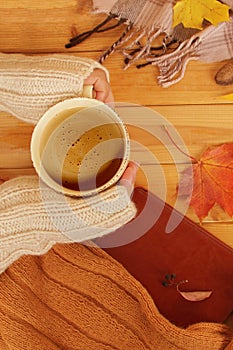 Cup of hot fragrant coffee in the hands of a woman, autumn leaves, an apple, cozy scarves and knitted sweaters, an e-book, flat,