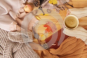 Cup of hot fragrant coffee in the hands of a woman, autumn leaves, an apple, cozy scarves and knitted sweaters, an e-book, flat,
