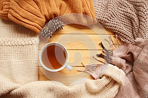 Cup of hot fragrant tea on a wooden background, autumn leaves, apple, cozy scarves and knitted sweaters, flat, concept hugge, photo