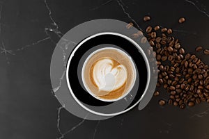 Cup of hot latte coffee with beautiful milk foam latte art texture with coffee bean on black marble background. Overhead