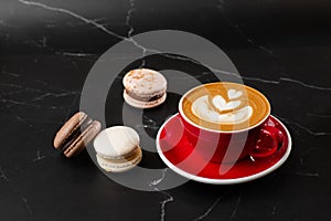 Cup of hot latte coffee with beautiful milk foam latte art texture with french macaroon on black marble background