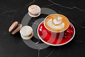 Cup of hot latte coffee with beautiful milk foam latte art texture with french macaroon on black marble background