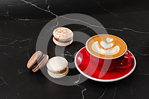 Cup of hot latte coffee with beautiful milk foam latte art texture with french macaroon on black marble background