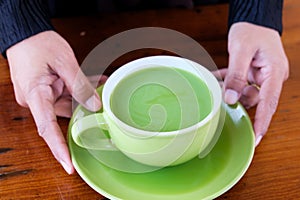 A Cup of Hot milk green tea in hands n the table photo