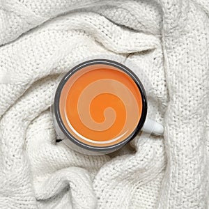 Cup of hot sea buckthorn tea on backdrop from white knitted sweater on a rustic wooden background. Immunization concept. Top view