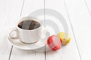 Cup of hot steaming coffe and two macaroons on a white wooden table. Sweet breakfast with delicious almond meringue cookies. High