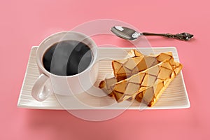 Cup of hot steaming coffee near phyllo puff pastries with an apricot glase on a white rectangular plate and spoon over pink