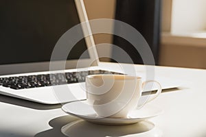 Cup of hot steaming morning coffee and laptop computer.