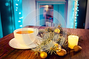 Cup of hot tea on a decorated table with candle and pine trees on a winter evening.