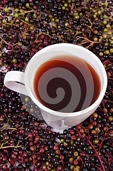 Cup of hot tea with elderberry juice and heap of berry, healthy nutrition