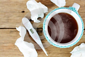 Cup of hot tea, paper wipes and thermometer on wooden table suggesting flu season photo