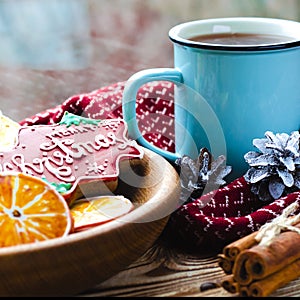 A cup of hot tea stands on a wooden table next to a wooden plate on which are gingerbread cookies made from orange slices against